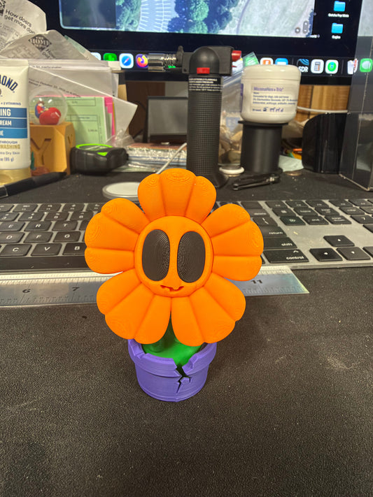 Orange flower figurine with oversized dark eyes, green stem and purple cracked-style pot, front view